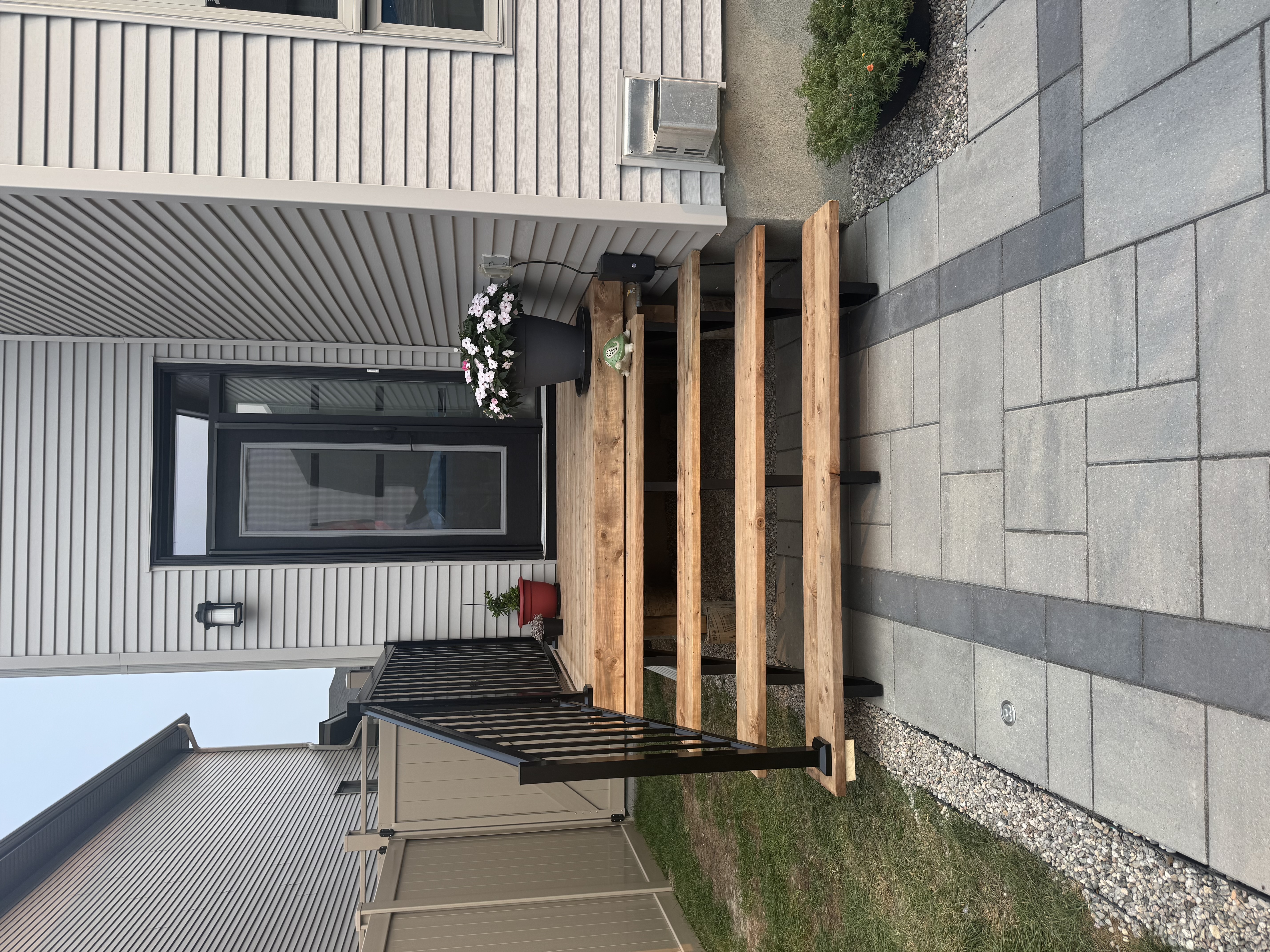 Wood deck stairs with black aluminum railings over interlock patio